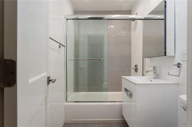 full bath featuring toilet, tile patterned floors, combined bath / shower with glass door, vanity, and tile walls