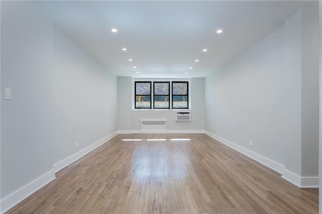 empty room with an AC wall unit, radiator heating unit, light wood-type flooring, and baseboards