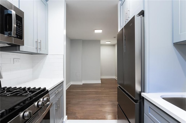 kitchen with gray cabinetry, decorative backsplash, appliances with stainless steel finishes, dark wood-type flooring, and baseboards