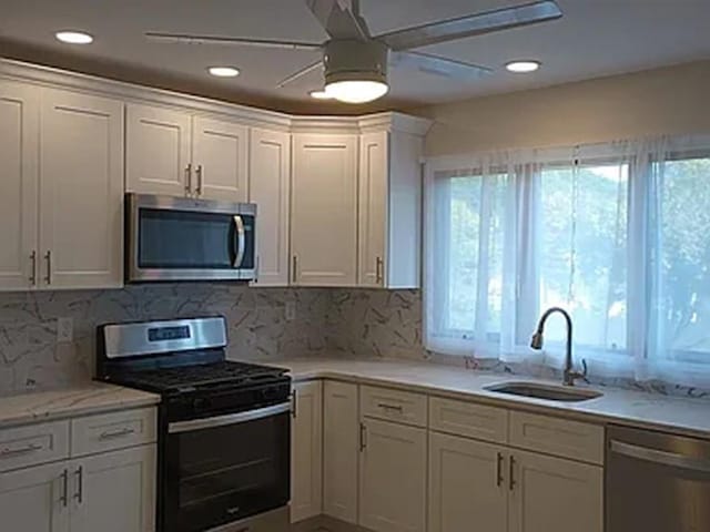 kitchen featuring appliances with stainless steel finishes, a sink, a wealth of natural light, and white cabinetry