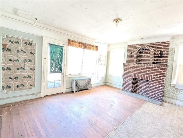 empty room featuring baseboards, wood-type flooring, a brick fireplace, and radiator heating unit