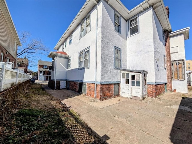 view of property exterior featuring stucco siding, brick siding, and fence