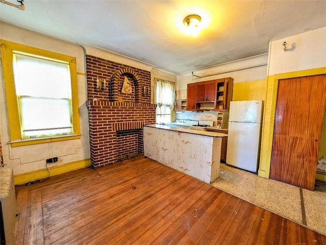 kitchen with open shelves, hardwood / wood-style floors, freestanding refrigerator, a peninsula, and brick wall