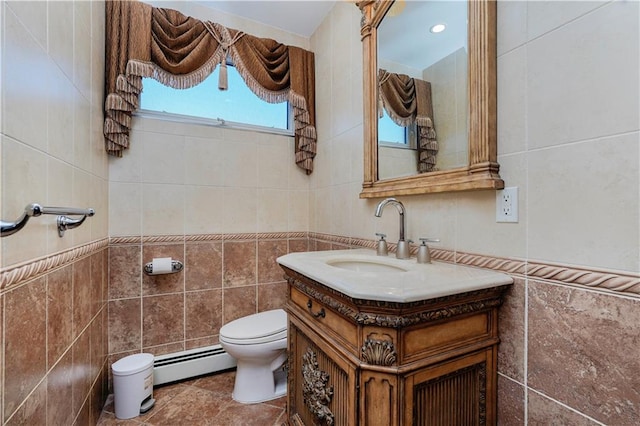 bathroom with a baseboard heating unit, toilet, vanity, and tile walls