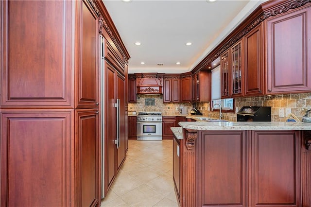 kitchen featuring a sink, high end stainless steel range oven, custom range hood, and dark brown cabinets