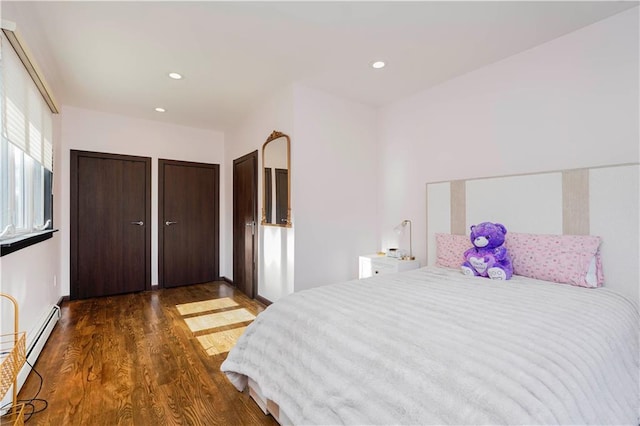 bedroom featuring baseboard heating, multiple closets, wood finished floors, and recessed lighting