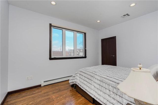 bedroom with baseboards, visible vents, wood finished floors, baseboard heating, and recessed lighting