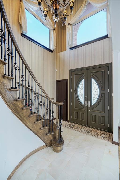 foyer with a high ceiling, stairway, a notable chandelier, and french doors