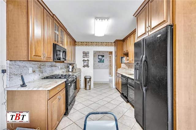 kitchen with light tile patterned floors, brown cabinetry, decorative backsplash, glass insert cabinets, and black appliances