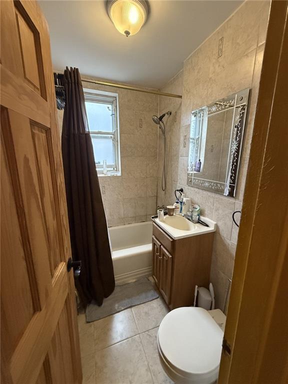 full bath featuring toilet, shower / tub combo with curtain, tile patterned floors, vanity, and tile walls