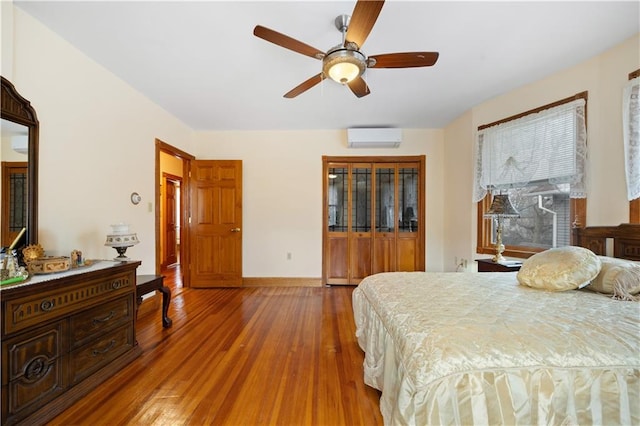 bedroom with a ceiling fan, wood-type flooring, a wall unit AC, and baseboards