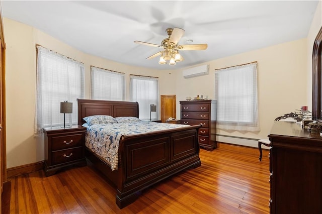 bedroom with a baseboard heating unit, a ceiling fan, baseboards, an AC wall unit, and hardwood / wood-style floors