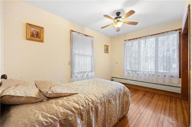 bedroom with a baseboard heating unit, wood-type flooring, and a ceiling fan