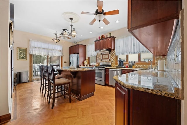 kitchen with decorative backsplash, radiator heating unit, appliances with stainless steel finishes, a sink, and a kitchen bar