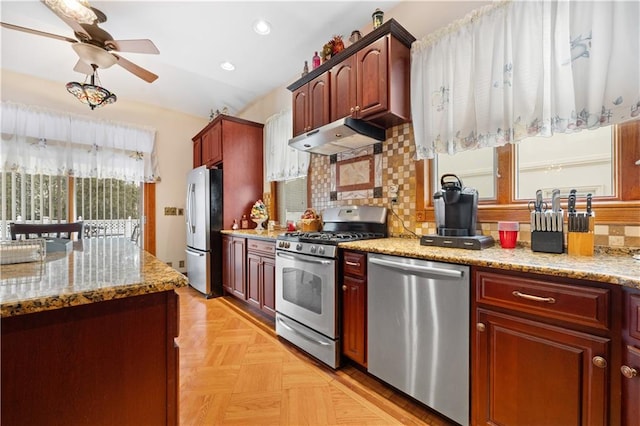 kitchen featuring under cabinet range hood, light stone counters, stainless steel appliances, and decorative backsplash