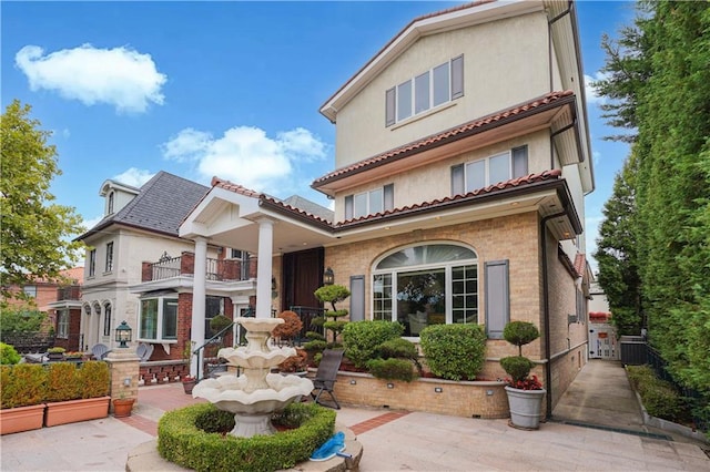 mediterranean / spanish-style house featuring a balcony, stucco siding, central air condition unit, and brick siding