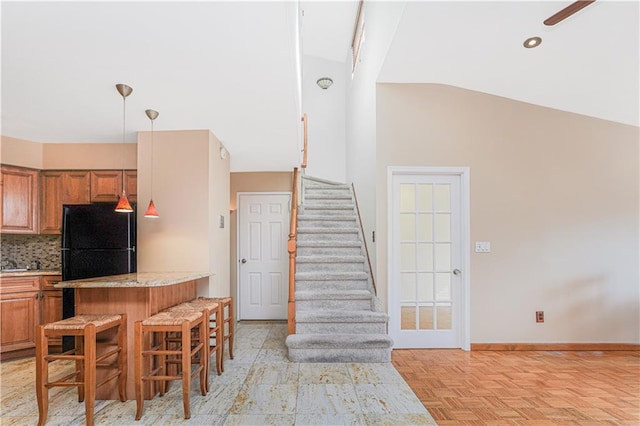 kitchen with brown cabinetry, decorative backsplash, a kitchen breakfast bar, freestanding refrigerator, and vaulted ceiling