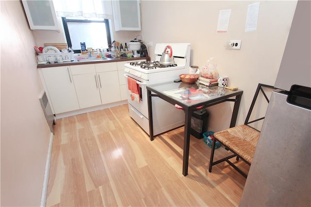 kitchen featuring white gas stove, light wood finished floors, a sink, and white cabinets