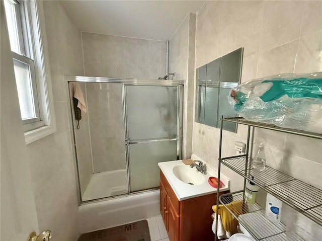 full bath featuring a shower with door, tile patterned flooring, tile walls, and vanity