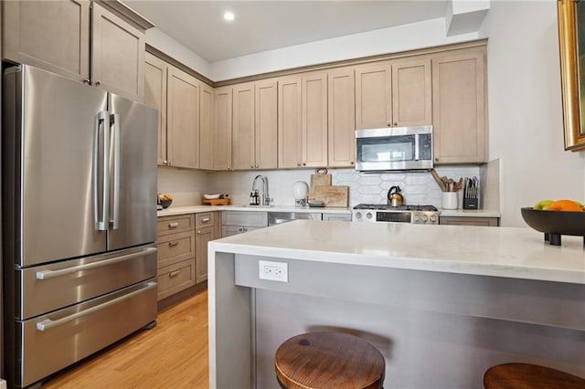 kitchen with a kitchen breakfast bar, backsplash, appliances with stainless steel finishes, light wood finished floors, and light stone countertops