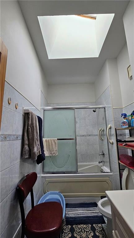 full bathroom featuring tile walls, a skylight, toilet, and bath / shower combo with glass door