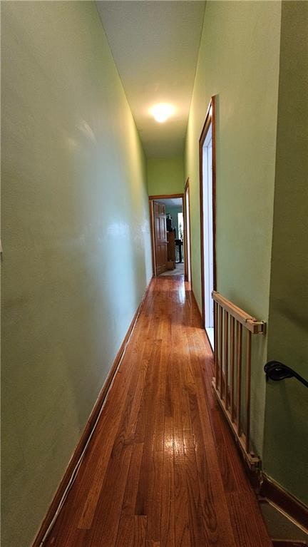 corridor featuring an upstairs landing, baseboards, and wood finished floors