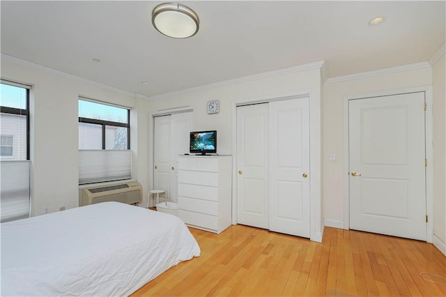 bedroom with a wall unit AC, light wood-type flooring, ornamental molding, and multiple closets