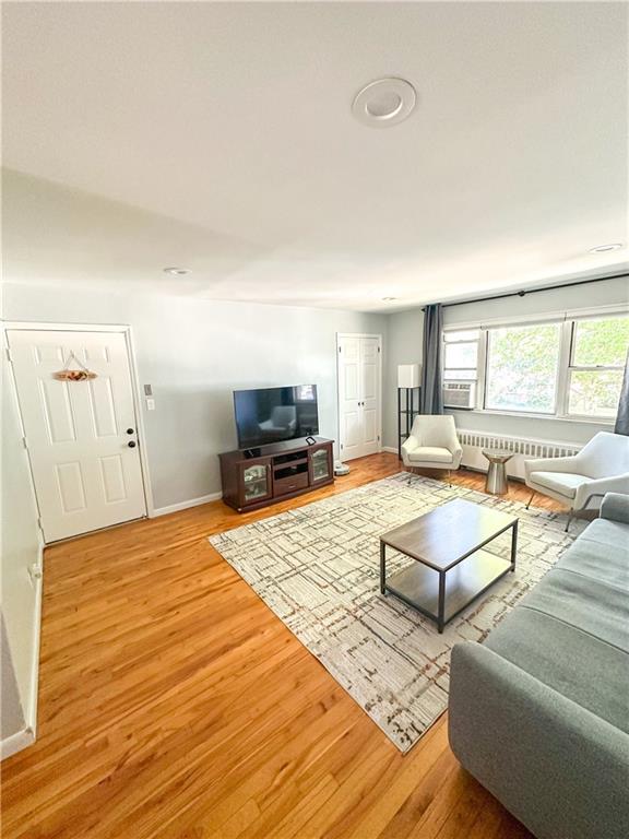 living room featuring radiator heating unit, cooling unit, wood finished floors, and baseboards