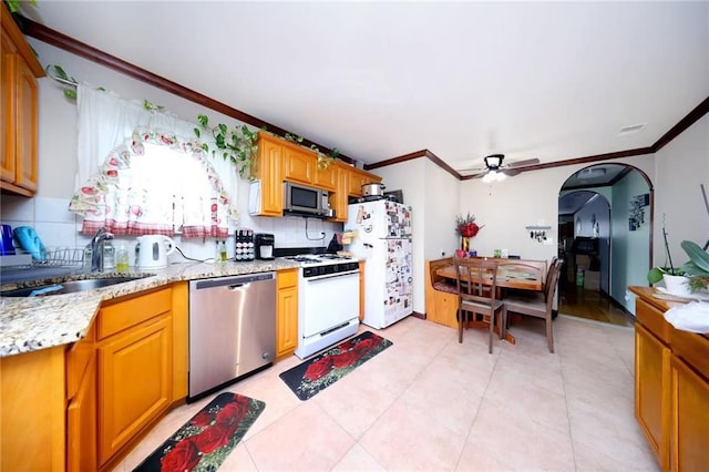 kitchen featuring arched walkways, crown molding, decorative backsplash, appliances with stainless steel finishes, and a sink