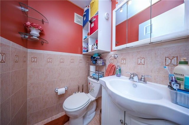 half bath with toilet, a wainscoted wall, a sink, visible vents, and tile walls