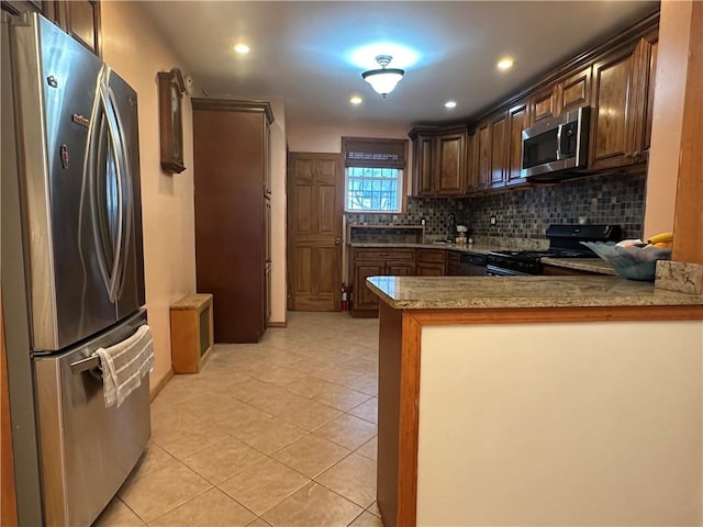 kitchen featuring light tile patterned floors, stainless steel appliances, a peninsula, dark brown cabinets, and backsplash