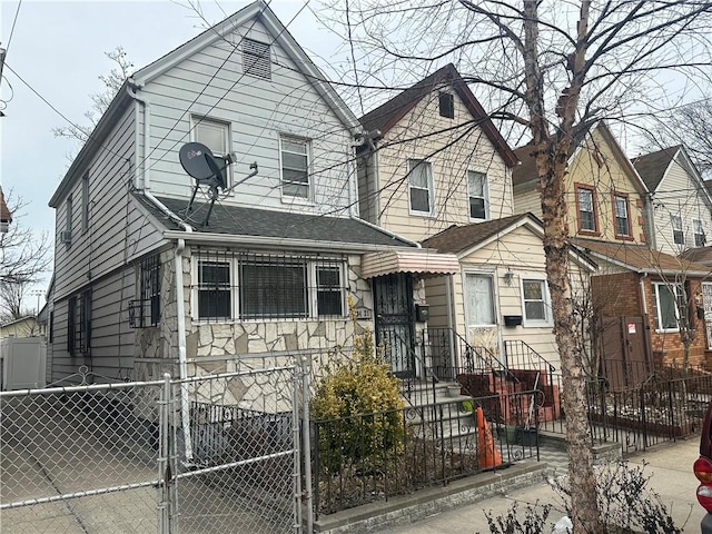 view of front of property with a gate, stone siding, a fenced front yard, and a shingled roof