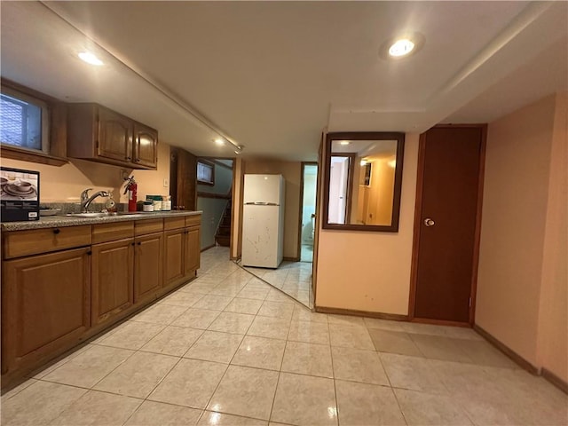 kitchen featuring light tile patterned floors, baseboards, freestanding refrigerator, a sink, and recessed lighting