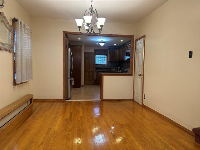 interior space featuring a baseboard heating unit, a notable chandelier, light wood-style flooring, and baseboards