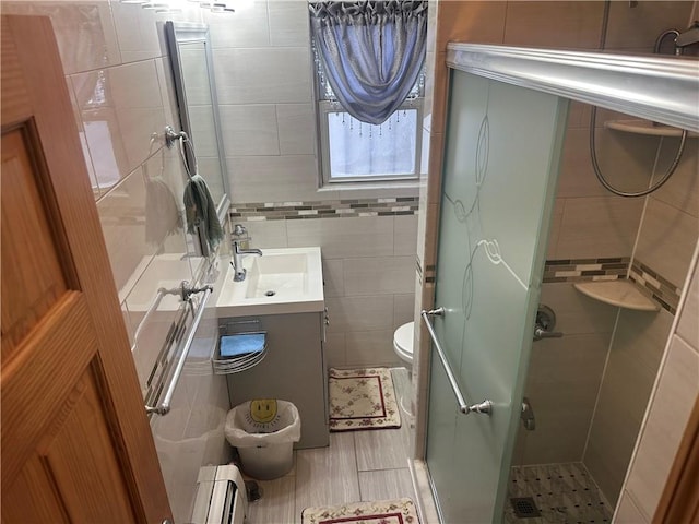 full bathroom featuring tile walls, a baseboard radiator, toilet, a stall shower, and vanity