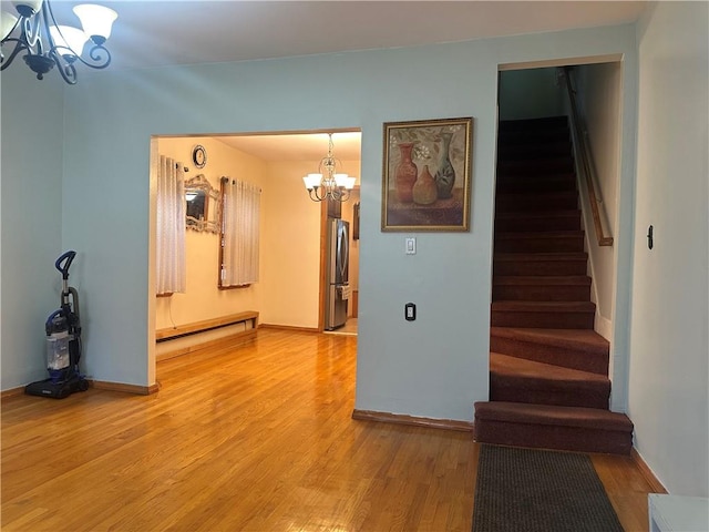 interior space featuring a notable chandelier, a baseboard heating unit, light wood-style floors, baseboards, and stairway