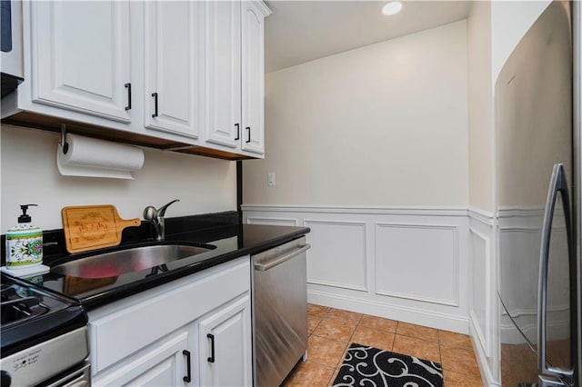 kitchen featuring a wainscoted wall, stainless steel appliances, white cabinetry, a sink, and light tile patterned flooring