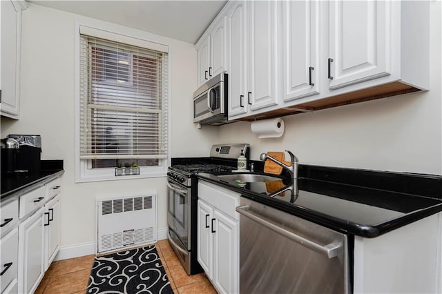 kitchen featuring dark countertops, radiator heating unit, appliances with stainless steel finishes, and white cabinets