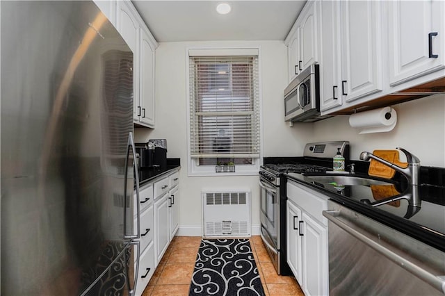 kitchen with light tile patterned floors, dark countertops, radiator heating unit, appliances with stainless steel finishes, and white cabinets