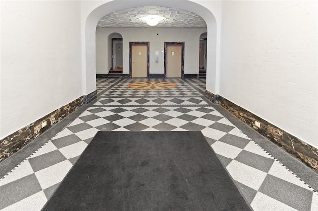 hallway featuring arched walkways, baseboards, and tile patterned floors