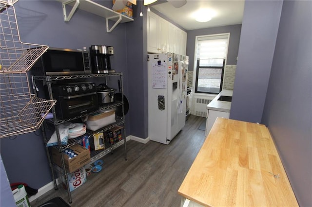 kitchen featuring radiator, wood finished floors, white fridge with ice dispenser, white cabinetry, and stainless steel microwave