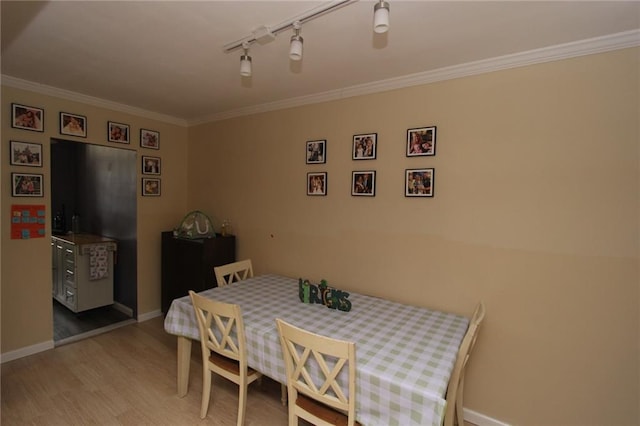 dining room featuring rail lighting, baseboards, light wood-style floors, and ornamental molding