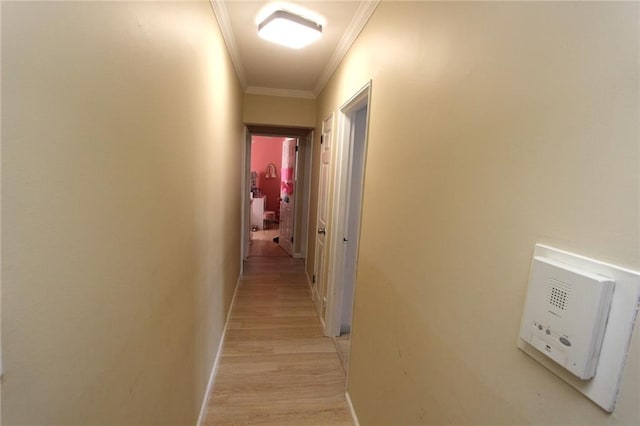 hallway featuring baseboards, crown molding, and light wood-style floors