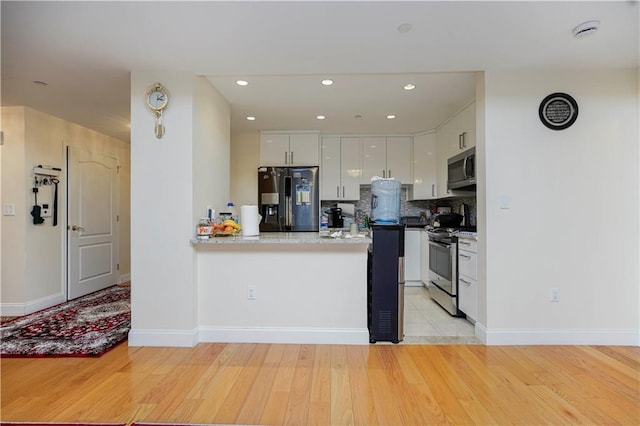 kitchen featuring tasteful backsplash, a peninsula, light wood-style floors, white cabinets, and stainless steel appliances