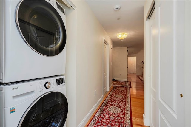 clothes washing area featuring baseboards, light wood-style flooring, laundry area, and stacked washer / dryer