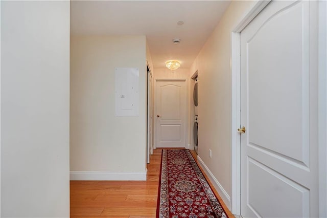 hallway with electric panel, baseboards, stacked washer and clothes dryer, and light wood-style flooring