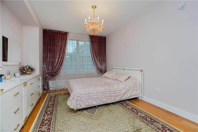 bedroom with light wood-style flooring, an inviting chandelier, and baseboards