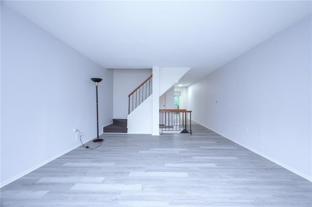 unfurnished room featuring light wood-type flooring, stairway, and baseboards