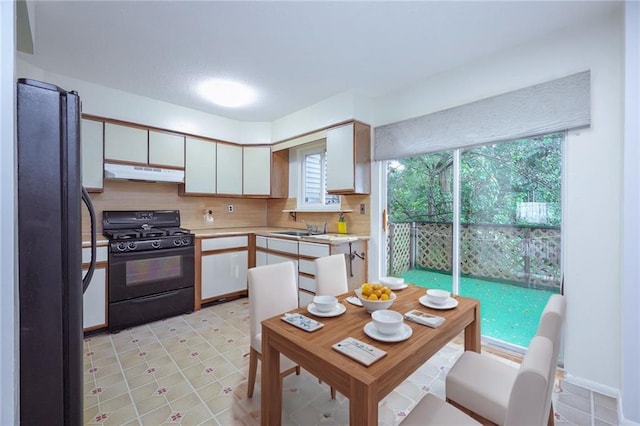 kitchen with decorative backsplash, under cabinet range hood, light countertops, black appliances, and a sink