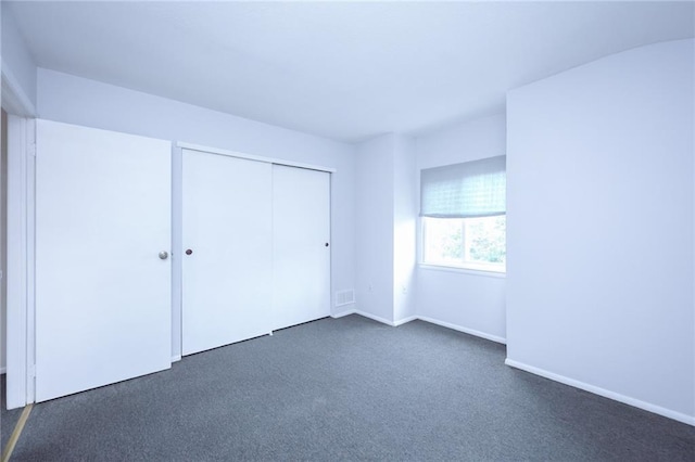 unfurnished bedroom with baseboards, visible vents, dark carpet, and a closet